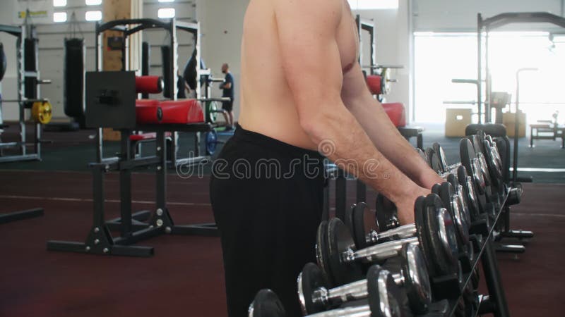 肌肉运动男运动员在健身中从支架上选择哑铃.