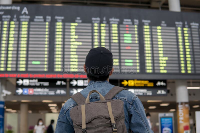 背着背包戴帽子、望着机场航站楼出发牌的年轻男旅客. 男性游客