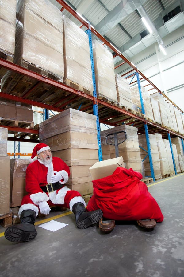 Overworked santa claus with pain in chest with list of gifts to buy in storehouse. Overworked santa claus with pain in chest with list of gifts to buy in storehouse