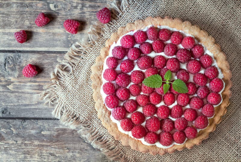 Homemade traditional sweet raspberry tart pie with cream and mint on vintage wooden table background. Rustic style and natural light. Homemade traditional sweet raspberry tart pie with cream and mint on vintage wooden table background. Rustic style and natural light.