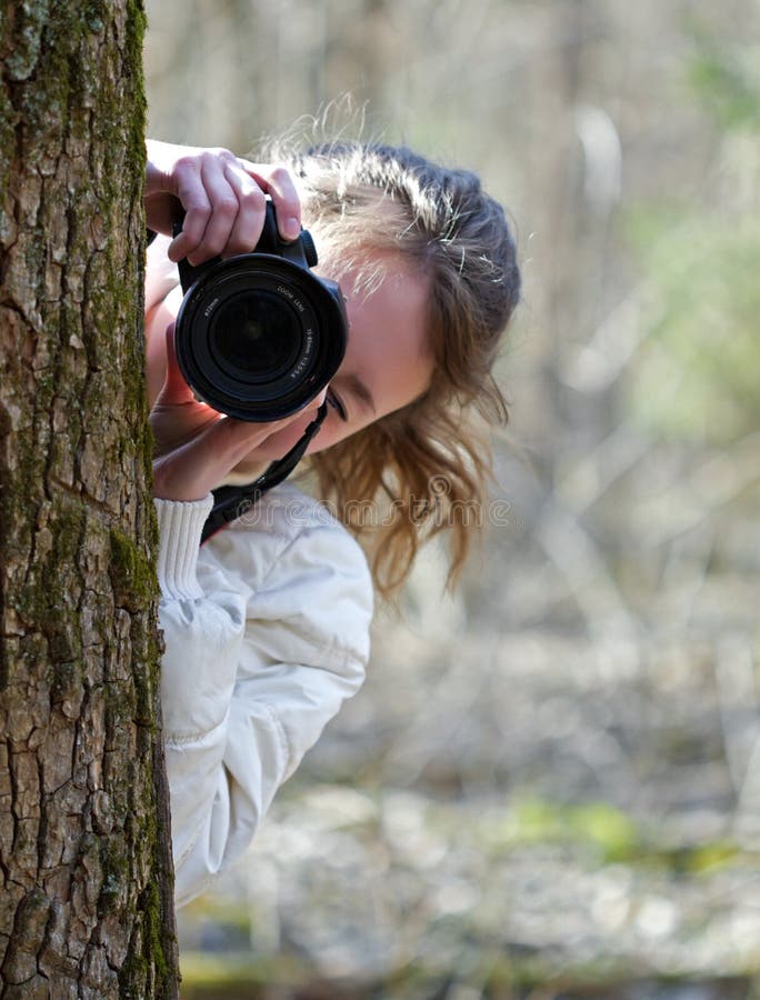 Portrait of nature photographer young woman. The girl is shooting you (camera towarded to you) in a spring day sunny forest. Portrait of nature photographer young woman. The girl is shooting you (camera towarded to you) in a spring day sunny forest.