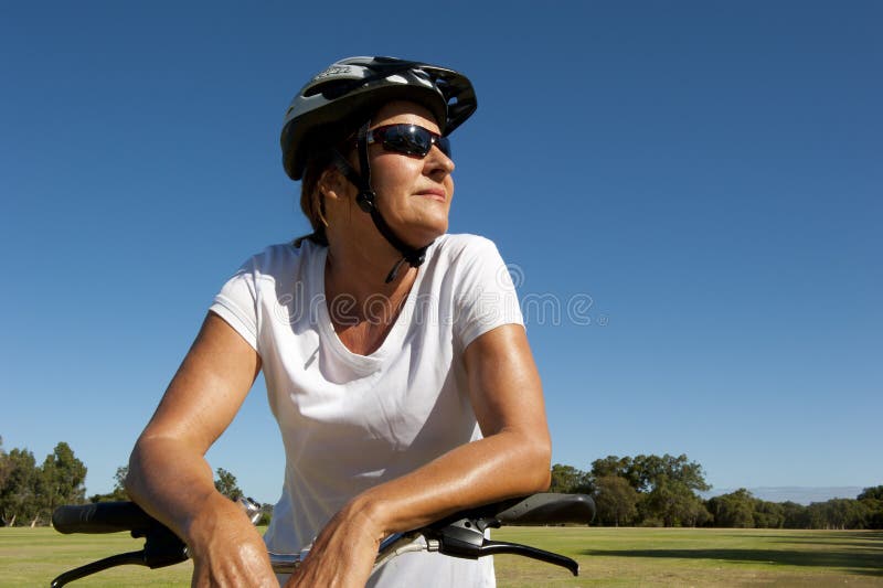 An attractive looking mature woman keeps herself fit and healthy with a bike ride. Upward view and spotless blue sky as background and copy space. An attractive looking mature woman keeps herself fit and healthy with a bike ride. Upward view and spotless blue sky as background and copy space.