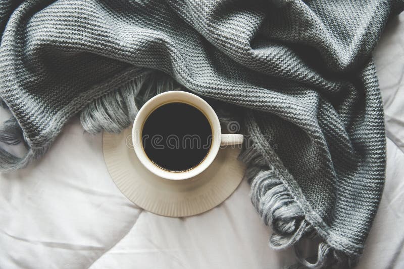 舒适冬天家庭背景，杯子热的咖啡用蛋白软糖，温暖在白色床背景，葡萄酒口气的被编织的毛线衣