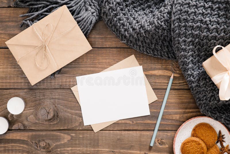 Cozy home desk, hygge, autumn fall concept. Blank paper card mockup, craft envelope, cookies, candles, women fashion scarf, gift box on wooden background. Flat lat, top view, copy space. Cozy home desk, hygge, autumn fall concept. Blank paper card mockup, craft envelope, cookies, candles, women fashion scarf, gift box on wooden background. Flat lat, top view, copy space