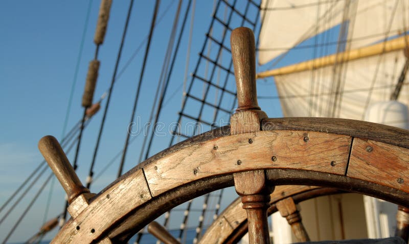 Wooden steering wheel against sails. Wooden steering wheel against sails