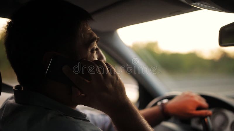 英俊的年轻人谈话在手机，当驾驶他的汽车时 危险，冒失驾驶员恶习 交通安全