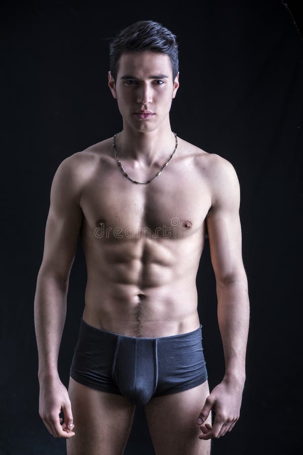 Handsome, fit young man wearing only underwear standing on black background, looking at camera. Handsome, fit young man wearing only underwear standing on black background, looking at camera