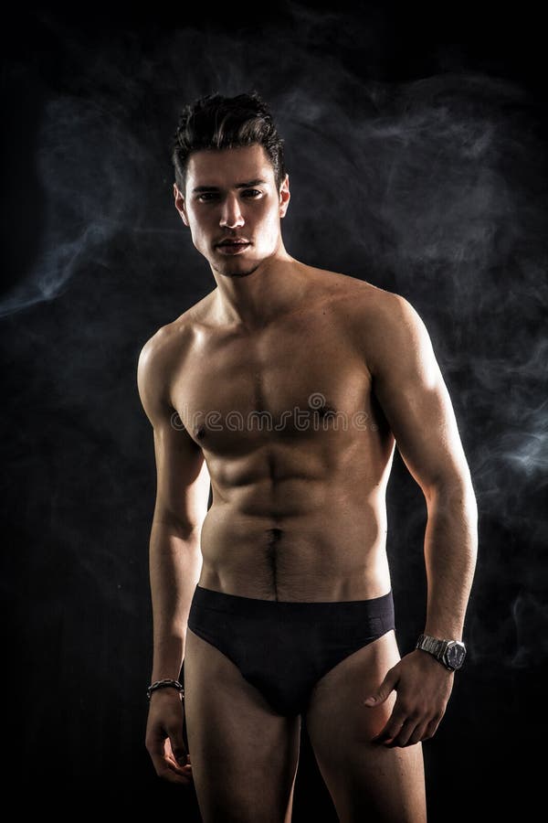 Handsome, fit young man wearing only underwear standing on black background, looking at camera. Handsome, fit young man wearing only underwear standing on black background, looking at camera
