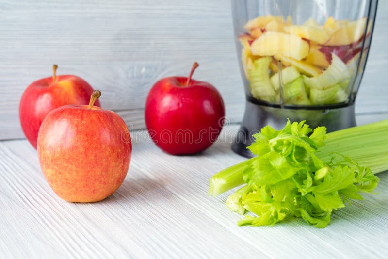 Apples, a bunch of celery, and a food processor on white table. Concept of healthy nutrition. Apples, a bunch of celery, and a food processor on white table. Concept of healthy nutrition.