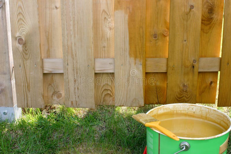 Half painted fence with paintbrush on the paint bucket. Half painted fence with paintbrush on the paint bucket