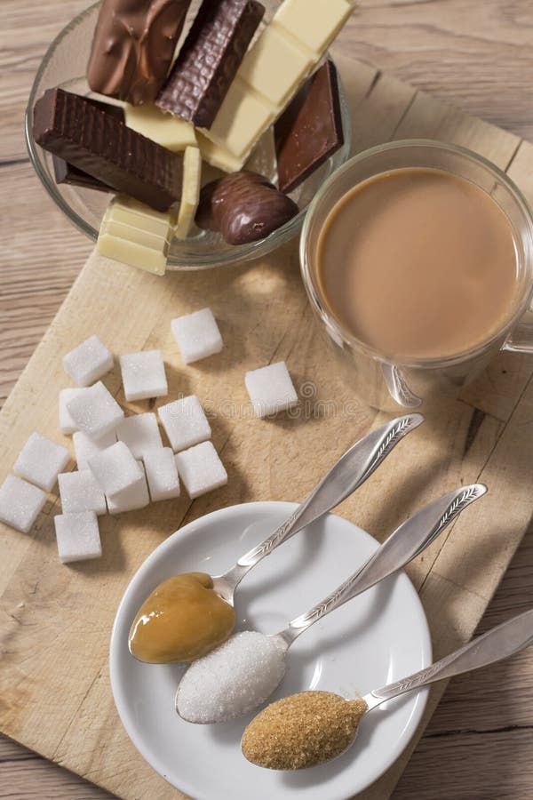 茶匙上的块糖、蔗糖、白糖和荞麦蜜，就放在加咖啡和牛奶的玻璃杯旁边 在后面