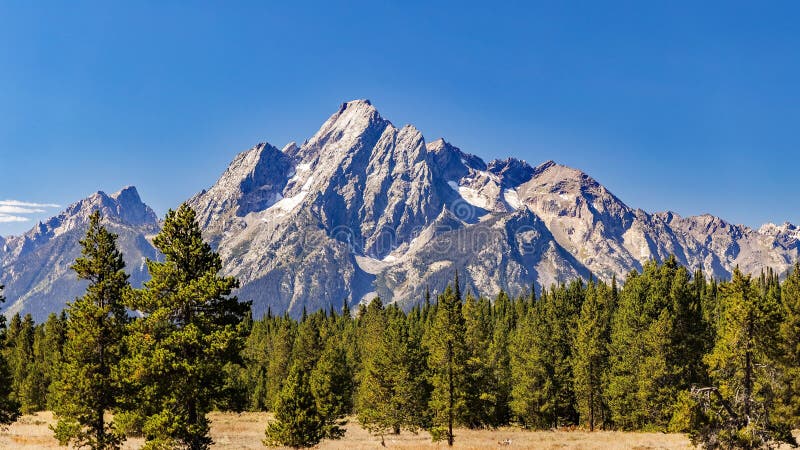 Majestic Mount Moran with its jagged peaks and small glaciers on a clear September day with a deep haze on the horizon from unchecked Canadian Forest Fires. The slopes are covered in alpine fir and subalpine fir trees up to the harsh environment of the tree line above which only rocks occur. While the flats below and across Jackson Lake are covered in grasses and timber of Lodgepole pine and spruce varieties. Majestic Mount Moran with its jagged peaks and small glaciers on a clear September day with a deep haze on the horizon from unchecked Canadian Forest Fires. The slopes are covered in alpine fir and subalpine fir trees up to the harsh environment of the tree line above which only rocks occur. While the flats below and across Jackson Lake are covered in grasses and timber of Lodgepole pine and spruce varieties.