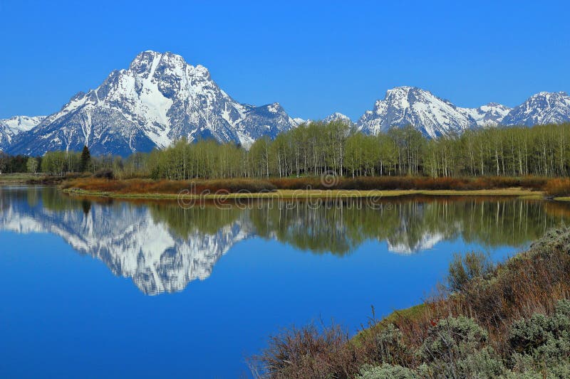 The sheer peaks of the Grand Teton Range and Mount Moran in the Rocky Mountains are reflected in the still waters of the oxbow bend of the Snake River in Grand Teton National Park, Wyoming, USA. The sheer peaks of the Grand Teton Range and Mount Moran in the Rocky Mountains are reflected in the still waters of the oxbow bend of the Snake River in Grand Teton National Park, Wyoming, USA.