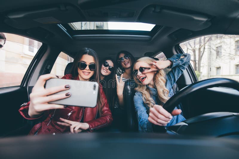 获得乐趣在汽车和采取与照相机的小组女孩selfies在旅行