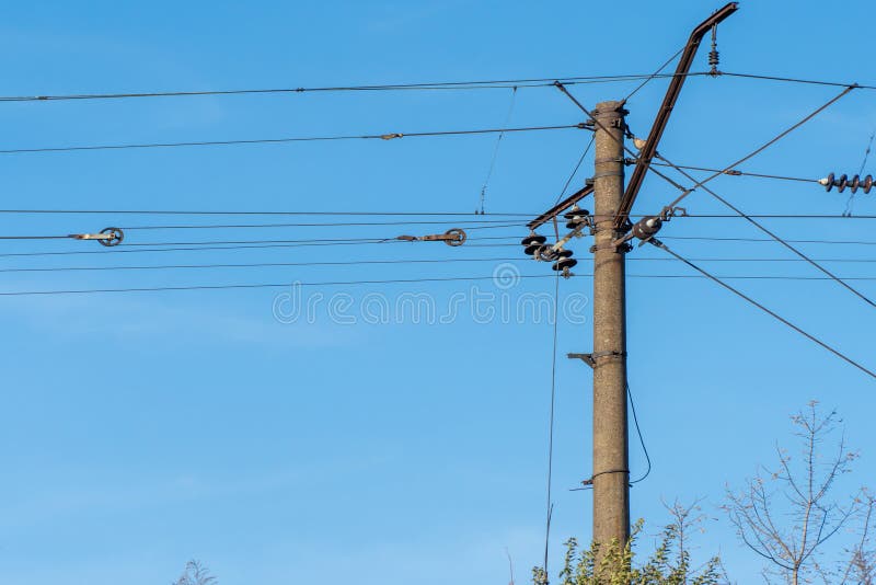 Electrified railway pole on blue sky background. Electric power supply lines on pillars along railway track. Technology of catenary wires. Details structure of voltage system. Equipment of railroad. Electrified railway pole on blue sky background. Electric power supply lines on pillars along railway track. Technology of catenary wires. Details structure of voltage system. Equipment of railroad.