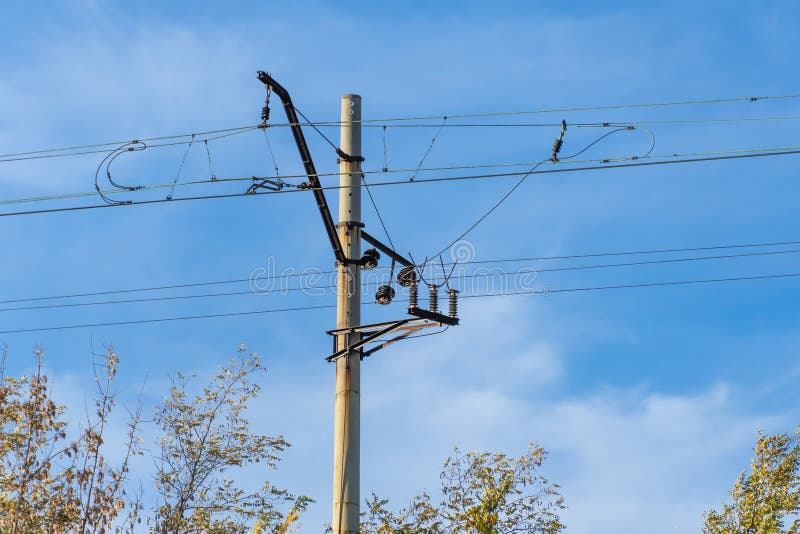 Electrified railway pole on blue sky background. Electric power supply lines on pillars along railway track. Technology of catenary wires. Details structure of voltage system. Equipment of railroad. Electrified railway pole on blue sky background. Electric power supply lines on pillars along railway track. Technology of catenary wires. Details structure of voltage system. Equipment of railroad.