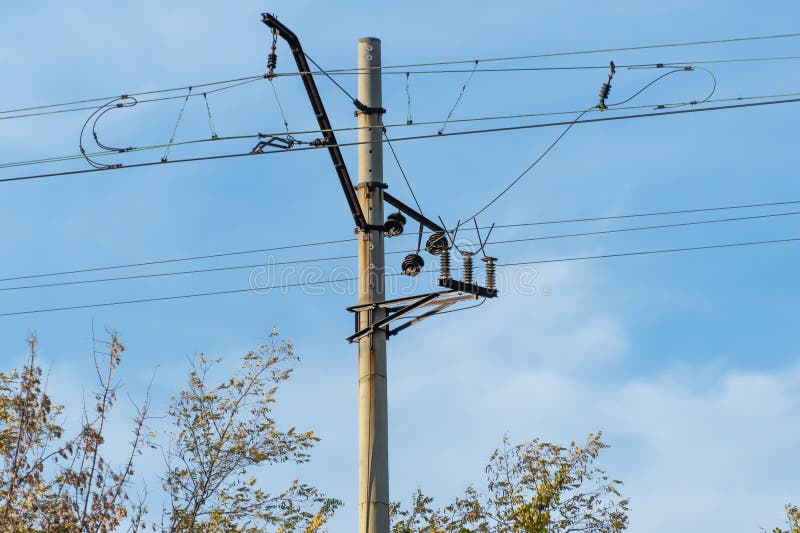 Electrified railway pole on blue sky background. Electric power supply lines on pillars along railway track. Technology of catenary wires. Details structure of voltage system. Equipment of railroad. Electrified railway pole on blue sky background. Electric power supply lines on pillars along railway track. Technology of catenary wires. Details structure of voltage system. Equipment of railroad.