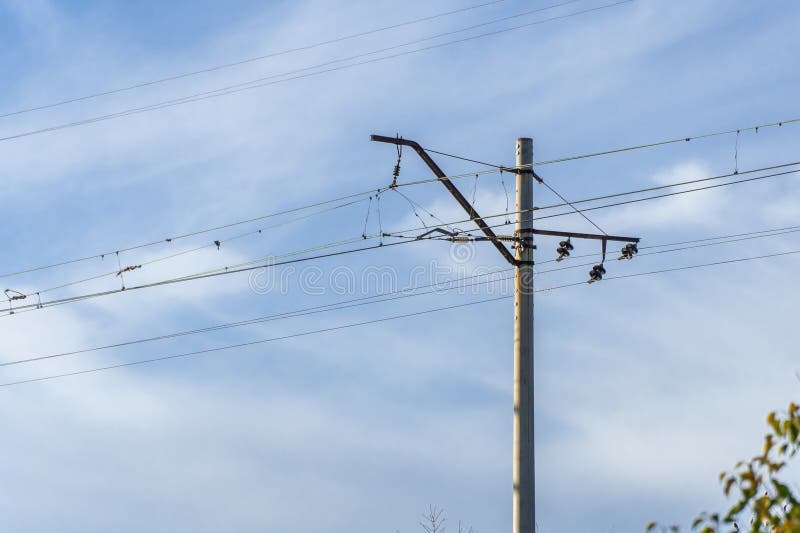 Electrified railway pole on blue sky background. Electric power supply lines on pillars along railway track. Technology of catenary wires. Details structure of voltage system. Equipment of railroad. Electrified railway pole on blue sky background. Electric power supply lines on pillars along railway track. Technology of catenary wires. Details structure of voltage system. Equipment of railroad.