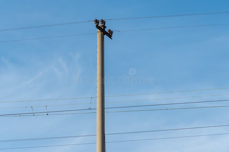 Electrified railway pole on blue sky background. Electric power supply lines on pillars along railway track. Technology of catenary wires. Details structure of voltage system. Equipment of railroad. Electrified railway pole on blue sky background. Electric power supply lines on pillars along railway track. Technology of catenary wires. Details structure of voltage system. Equipment of railroad.