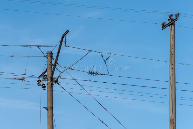 Electrified railway pole on blue sky background. Electric power supply lines on pillars along railway track. Technology of catenary wires. Details structure of voltage system. Equipment of railroad. Electrified railway pole on blue sky background. Electric power supply lines on pillars along railway track. Technology of catenary wires. Details structure of voltage system. Equipment of railroad.