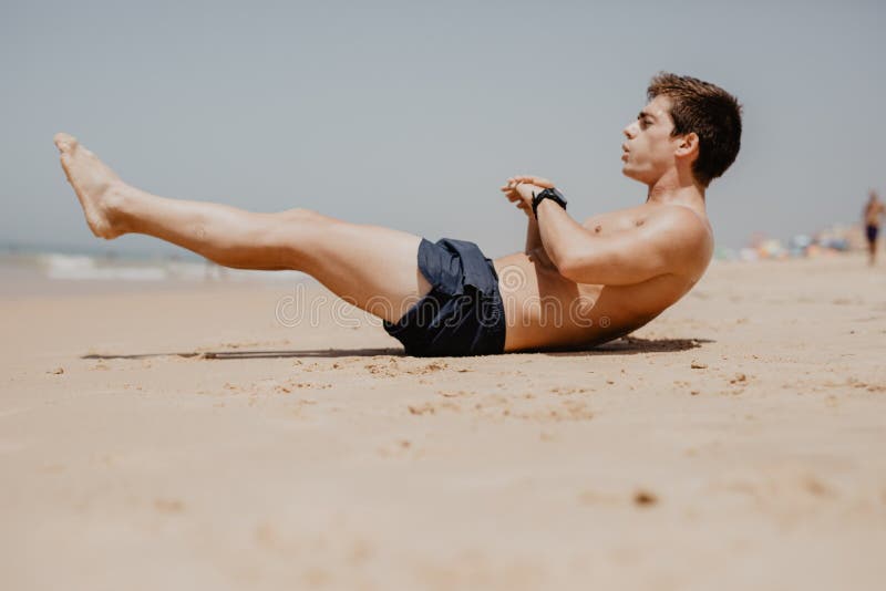 行使在海滩的一个年轻人的侧视图画象做仰卧起坐