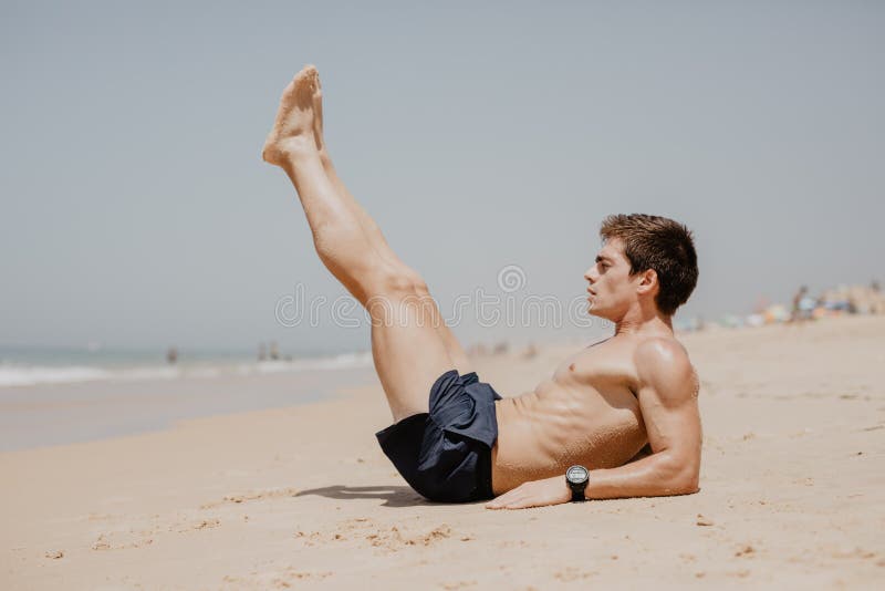 行使在海滩的一个年轻人的侧视图画象做仰卧起坐
