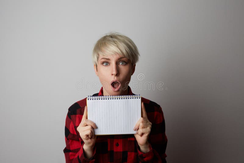 行家白肤金发的妇女画象摆在一件红色大笼子衬衣的拿着白色空的笔记薄和poiting吊 大模型 库存图片 行家白肤金发的妇女画象摆在一件红色大笼子衬衣的拿着白色空的笔记薄和poiting吊 大模型 库存图片