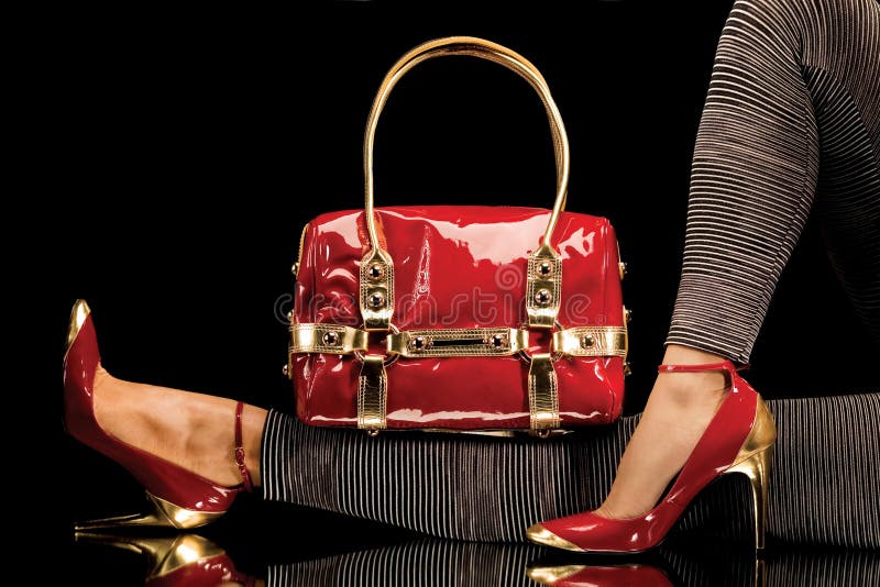 A close-up of a chic red handbag along with female legs wearing elegant red shoes. A close-up of a chic red handbag along with female legs wearing elegant red shoes.
