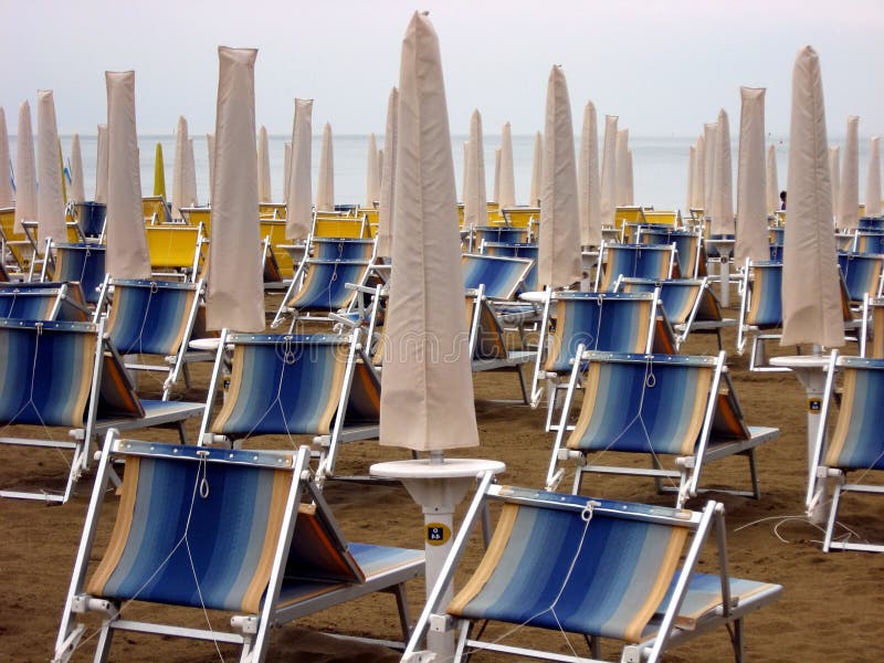 Sun beds and umbrellas closed in a deserted sandy beach in an Italian sea. Sun beds and umbrellas closed in a deserted sandy beach in an Italian sea