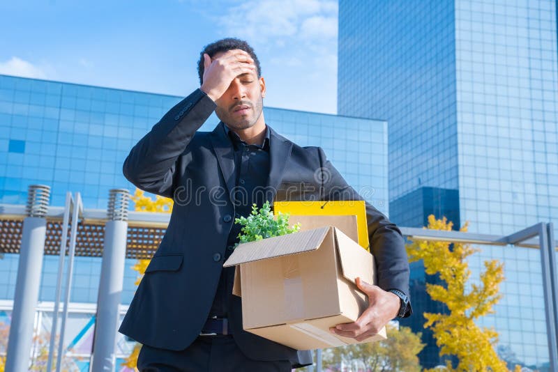 Man fired from his job unemployment concept. Dismissed employee on street carrying cardboard box with office stuff . High quality photo. Man fired from his job unemployment concept. Dismissed employee on street carrying cardboard box with office stuff . High quality photo