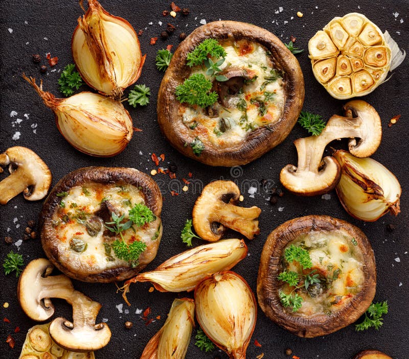 Baked portobello mushrooms stuffed with cheese and herbs on a black background, close-up, top view. Vegetarian food. Baked portobello mushrooms stuffed with cheese and herbs on a black background, close-up, top view. Vegetarian food