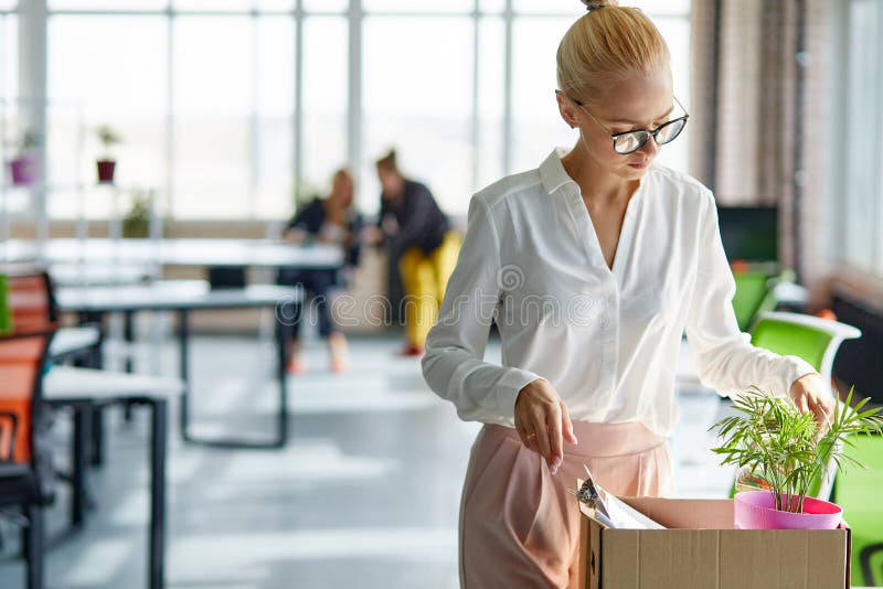 Sad dismissed female worker is taking her office supplies from office, packing in box. jobless female. Sad dismissed female worker is taking her office supplies from office, packing in box. jobless female