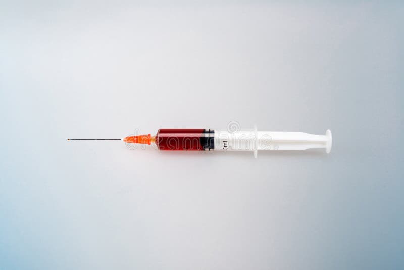 A syringe full of red liquid against a gray background that is about to be injected. A syringe full of red liquid against a gray background that is about to be injected