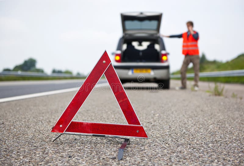 Warning tiangle behind a broken down car with a motorist calling for assistance. Focus on the triangle. Warning tiangle behind a broken down car with a motorist calling for assistance. Focus on the triangle