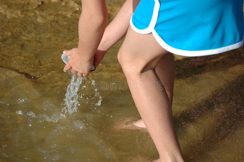 Little girl bends over to wash off shell in lake water. What uses water has. Little girl bends over to wash off shell in lake water. What uses water has.