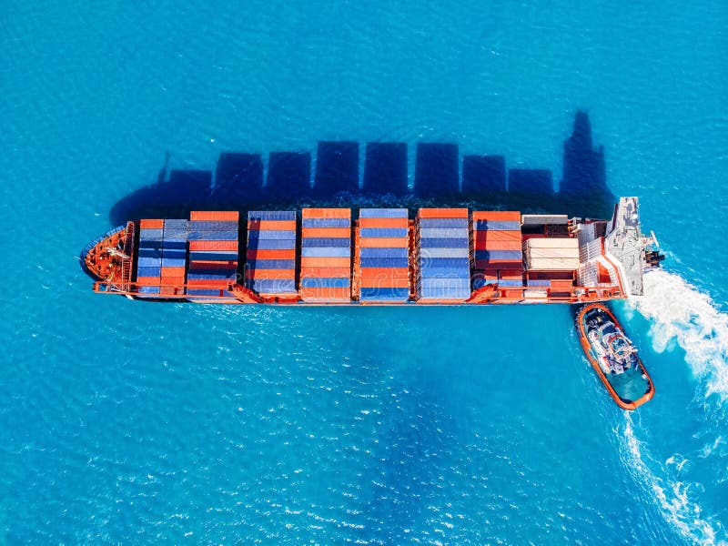 货轮进入贸易港口，拖船帮助靠泊码头。物流概念，海运 库存图片