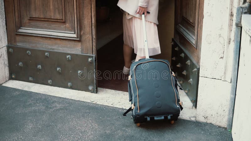 走带着在街道的一个手提箱的年轻旅客妇女 女孩打开门并且进入曲拱 免版税库存照片 走带着在街道的一个手提箱的年轻旅客妇女 女孩打开门并且进入曲拱 免版税库存照片
