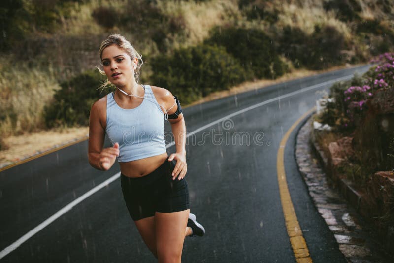 Fit young woman jogging outdoors on highway. Female athlete training running on a rainy day. Fit young woman jogging outdoors on highway. Female athlete training running on a rainy day.