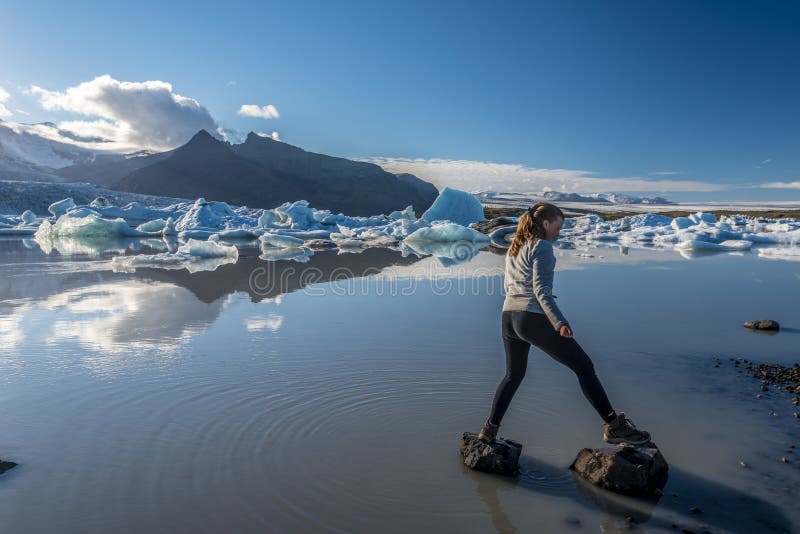 跳过在Fjallsarlon冰川湖边界的岩石的女孩少年 南冰岛 免版税库存照片 跳过在Fjallsarlon冰川湖边界的岩石的女孩少年 南冰岛 免版税库存照片