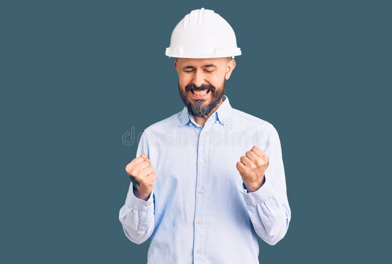 身着建筑师硬帽的年轻英俊男子举起双臂，闭上眼睛庆祝胜利 免版税库存图片