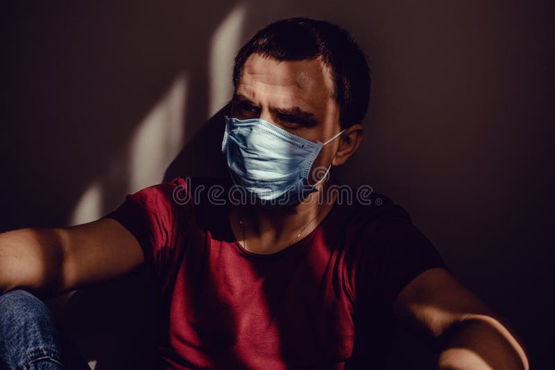 身穿医用面具的深思难耐的正人，坐在墙上，光影斑纹 保持隔离 免版税库存照片