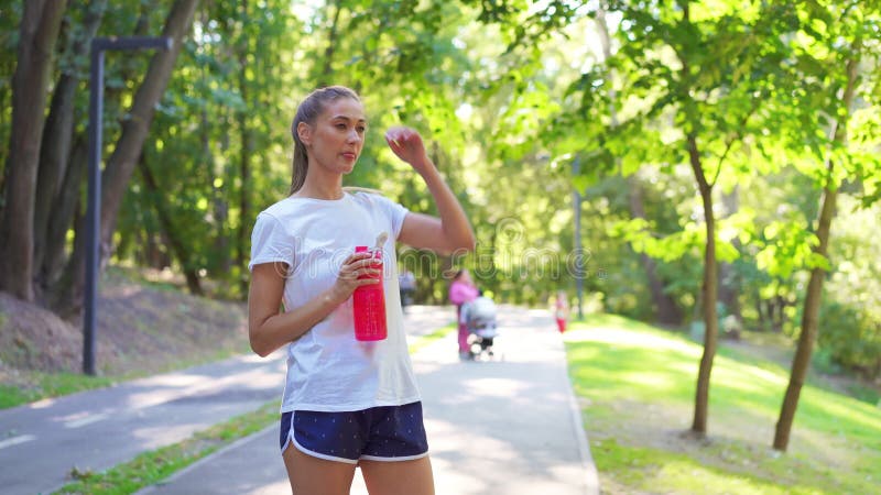 身穿运动服的疲惫女子在公园里的饮水中慢跑