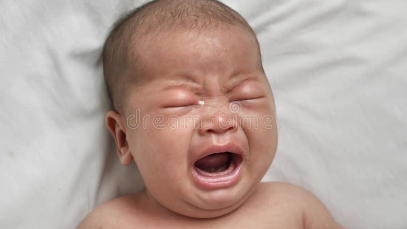 躺在床上哭泣的可爱亚洲新生儿的肖像