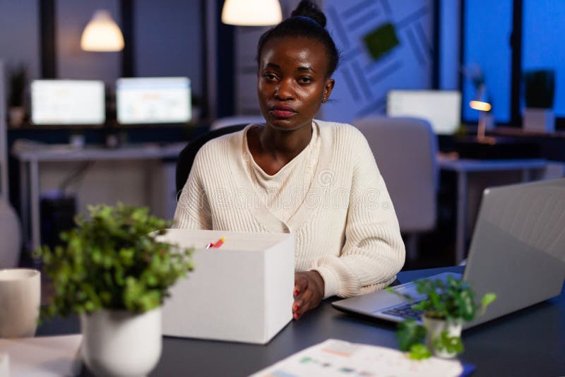 Portrait of resigned dismissed african american businesswoman packing objects after is fired late at night in startup company office. Black entrepreneur woman having business relocation problem. Portrait of resigned dismissed african american businesswoman packing objects after is fired late at night in startup company office. Black entrepreneur woman having business relocation problem