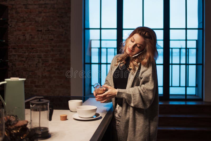 迷人的女孩在厨房里在早晨 谈话在电话和有有杯子的早餐A年轻女人在她的手上 库存照片 迷人的女孩在厨房里在早晨 谈话在电话和有有杯子的早餐A年轻女人在她的手上 库存照片