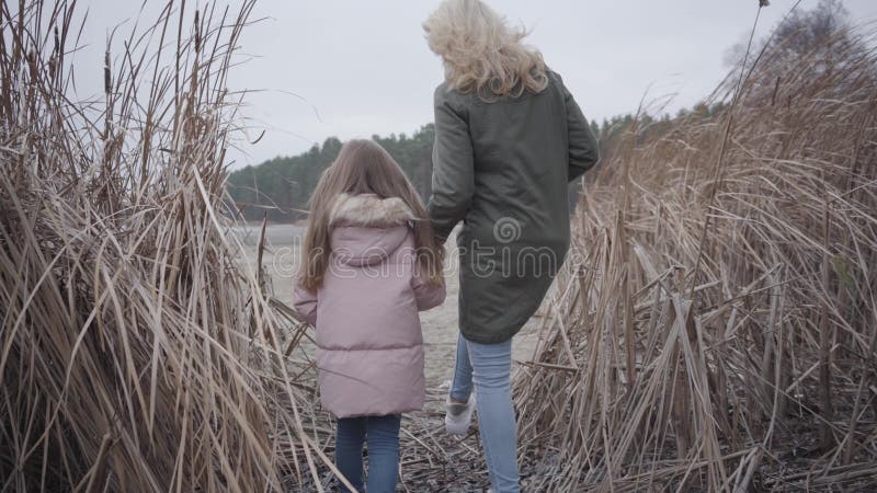 追踪白人成年女子和女孩在灌木丛中走向湖泊或河流的镜头 美丽的母亲和可爱 股票视频