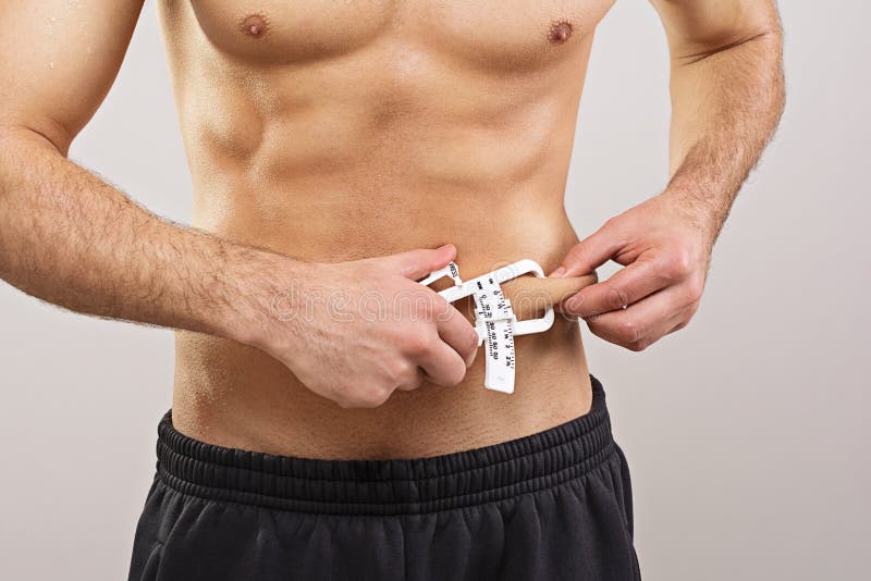 Closeup of fit young sportsman measuring body fat level using caliper. Diet, fitness, healthy lifestyle and body care concept. Closeup of fit young sportsman measuring body fat level using caliper. Diet, fitness, healthy lifestyle and body care concept.