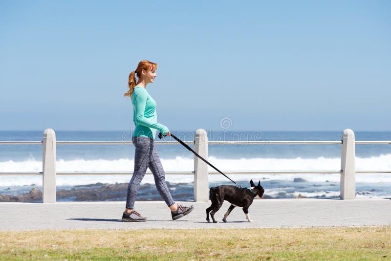 Full body portrait of fit woman smiling and walking dog on path by sea. Full body portrait of fit woman smiling and walking dog on path by sea
