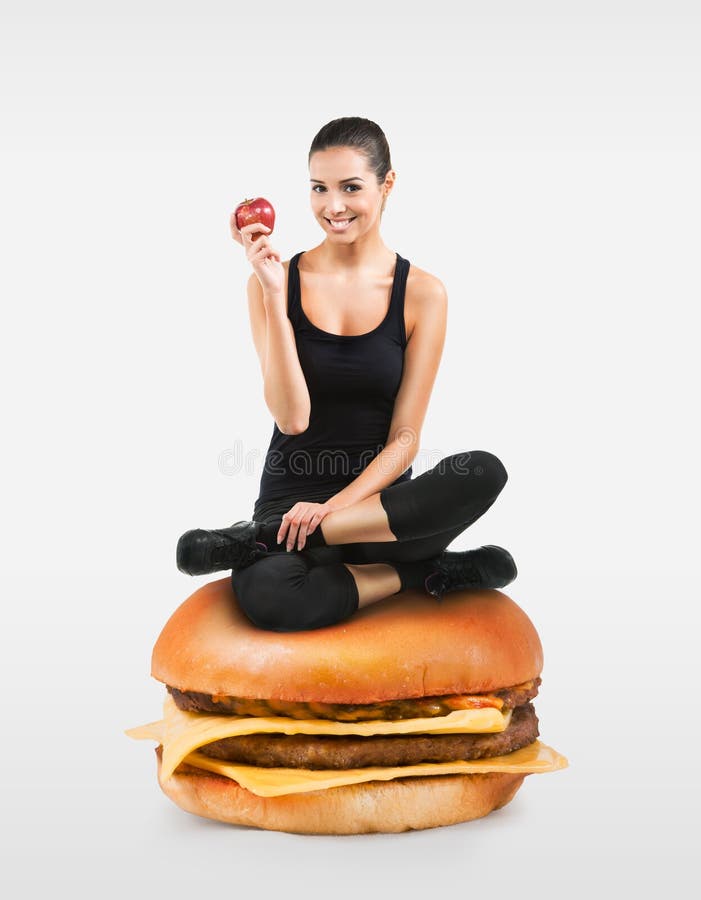 Beautiful fit girl sitting on a hamburger holding an apple. Beautiful fit girl sitting on a hamburger holding an apple