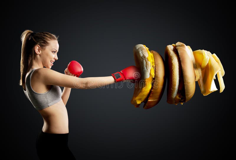 Fit, young, energetic woman boxing unhealthy food, black background. Fit, young, energetic woman boxing unhealthy food, black background